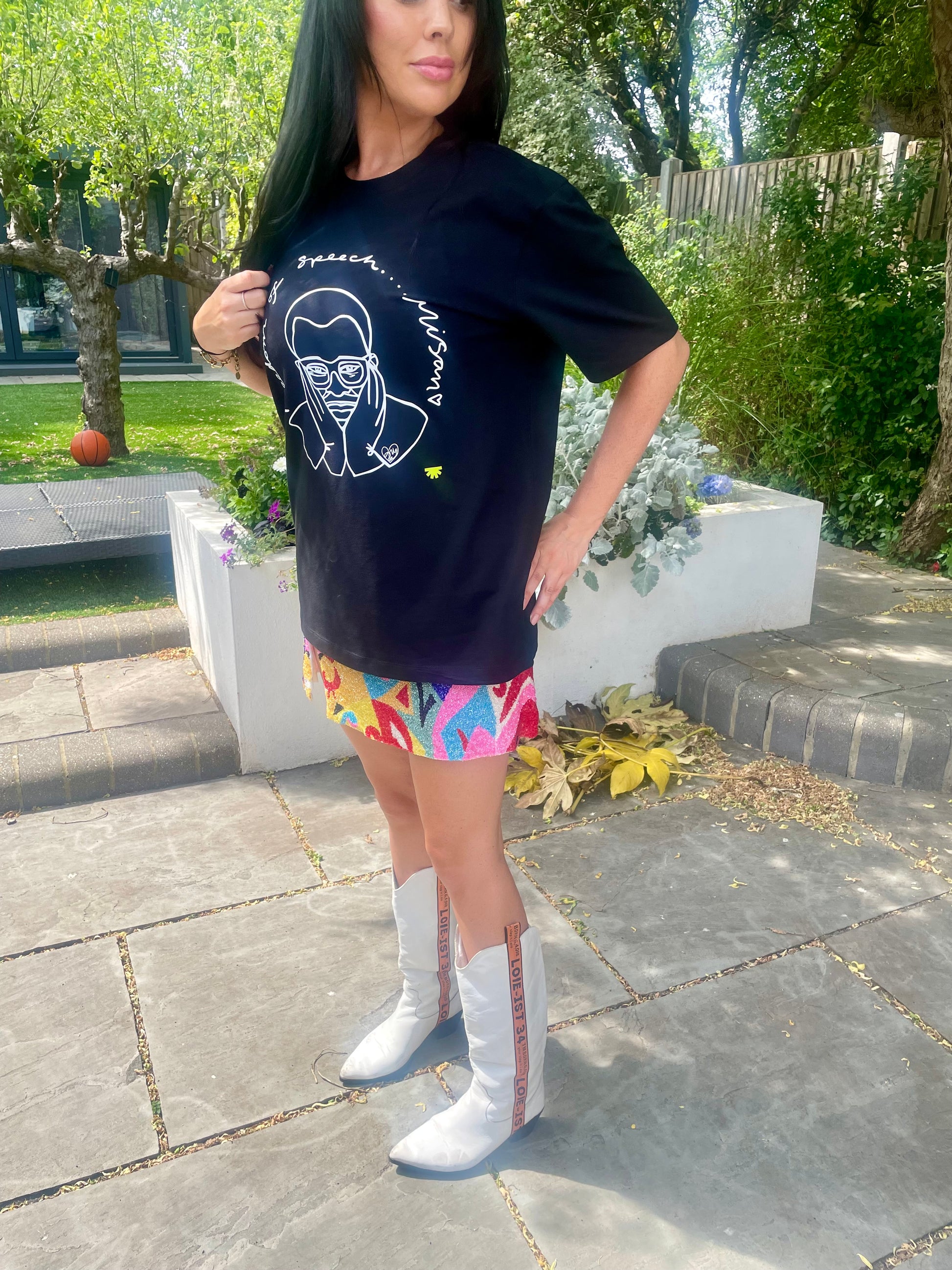 Woman wearing a black t-shirt with a graphic design, colorful shorts, and white boots outdoors.